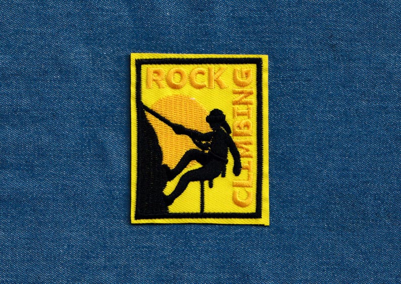 May include: Yellow and black embroidered patch with a silhouette of a person rock climbing with the text "ROCK CLIMBING" on a yellow background.
