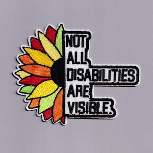 Può includere: Toppa ricamata con un design di girasole colorato e la scritta "NOT ALL DISABILITIES ARE VISIBLE". Il girasole ha petali nei toni del rosso, giallo e arancione. Il testo è nero.