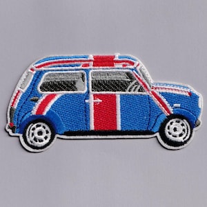Op de afbeelding: Geborduurde patch met een blauwe auto met rode en witte accenten en een Union Jack-ontwerp op het dak. De auto heeft zwarte wielen en een witte omtrek, tegen een lichtgrijze achtergrond. Een decoratief item.