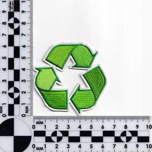May include: A green embroidered patch featuring the universal recycling symbol, a triangle of three chasing arrows. The patch has a white border and is set against a white background. The patch is approximately 2 inches in diameter.