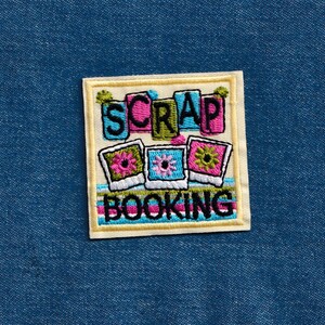 May include: A white and yellow embroidered patch with the text "Scrap Booking" and three colorful picture frames with flowers.
