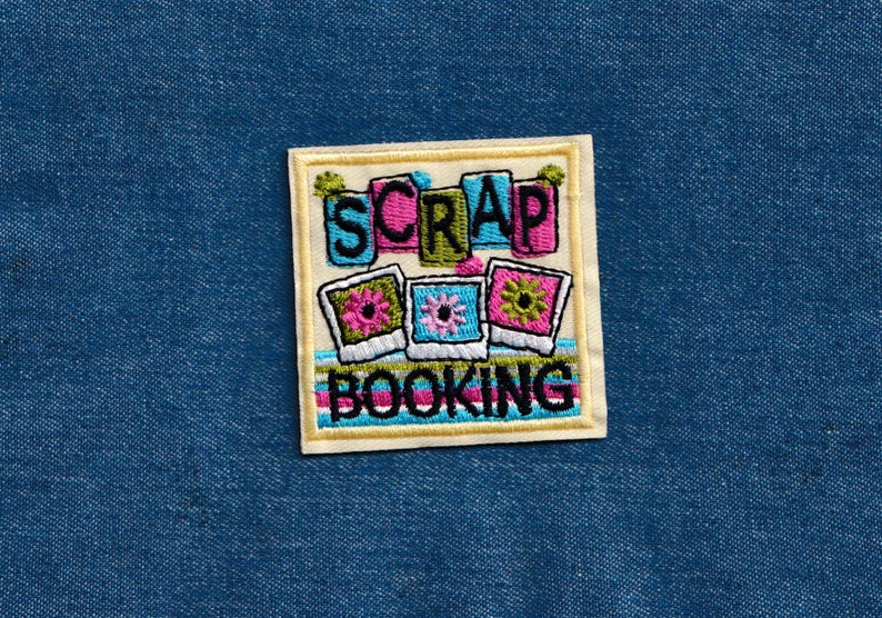 May include: A white and yellow embroidered patch with the text "Scrap Booking" and three colorful picture frames with flowers.
