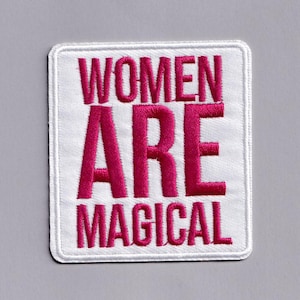 Può includere: Una toppa quadrata bianca ricamata con le parole "WOMEN ARE MAGICAL" in lettere maiuscole rosa acceso. La toppa ha un bordo bianco ed è posta su uno sfondo grigio.