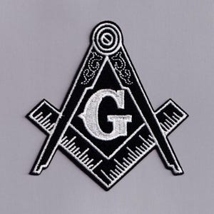 Könnte beinhalten: Schwarz-weißer, gestickter Aufnäher mit dem Freimaurer-Symbol von Winkel und Zirkel. Das Emblem enthält einen weißen Buchstaben "G" in der Mitte, umgeben von einem schwarzen Dreieck, Quadrat und linealartigen Elementen. Der Aufnäher befindet sich auf grauem Hintergrund.