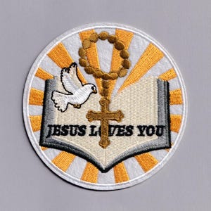 May include: Embroidered patch with a religious theme. The design features a dove, a cross, a rosary, and an open book with the text "JESUS LOVES YOU" in black. The patch has a white border with yellow and orange rays.