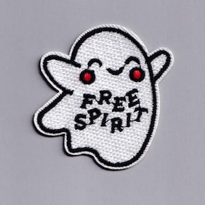 May include: Embroidered patch in the shape of a white ghost with a black outline. The ghost has red eyes and the words "FREE SPIRIT" in black. The patch is on a gray background.