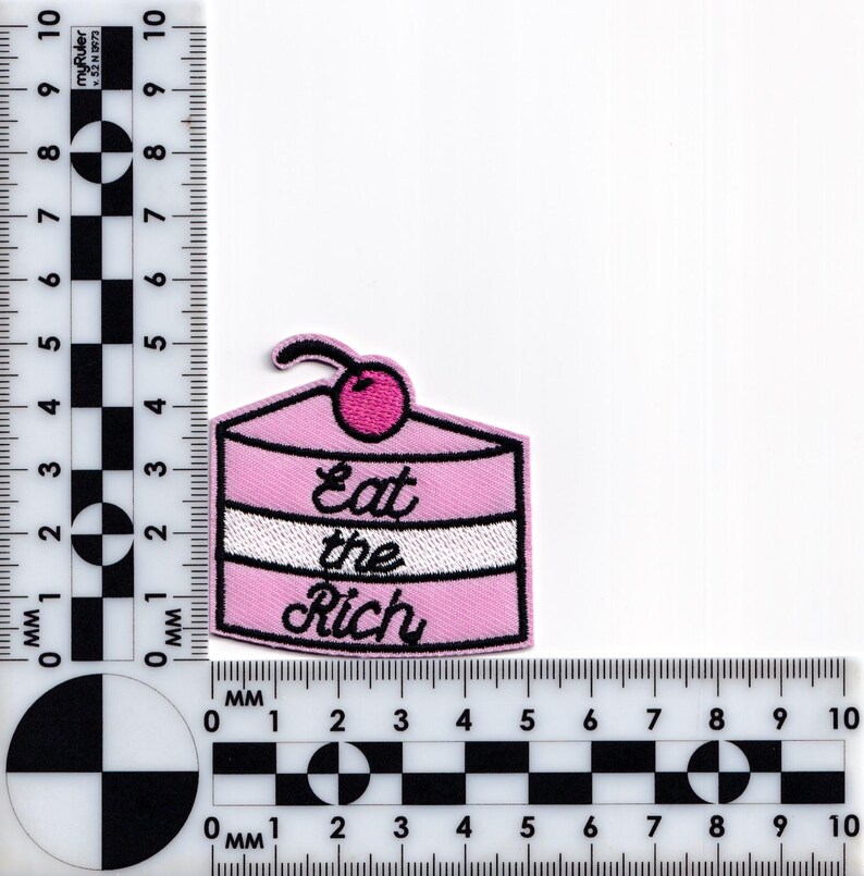 May include: Pink embroidered patch with a pink and white layered cake with a cherry on top. The text "Eat the Rich" is embroidered in black on the cake.