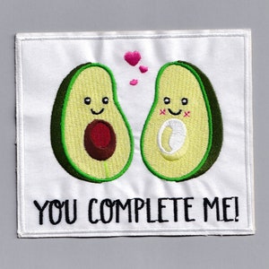 May include: White embroidered patch featuring two avocado halves, each with a smiling face. The avocado halves are facing each other and have pink hearts above them. The text "YOU COMPLETE ME!" is below the avocados.