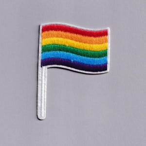 Può includere: Toppa ricamata con il design della bandiera arcobaleno. La bandiera presenta strisce orizzontali rosse, arancioni, gialle, verdi, blu e viola. È montata su un'asta bianca, con un bordo bianco. La toppa è su sfondo grigio.