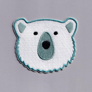 Puede incluir: Parche bordado con la cabeza de un oso polar. El oso tiene una cara blanca con una nariz y orejas color turquesa y ojos negros. El parche está delineado con costuras turquesas y tiene un borde festoneado. El parche está sobre un fondo gris.