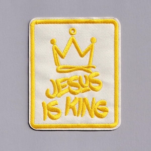 May include: Embroidered patch with a white background and a yellow border. The patch features a yellow crown design above the words "JESUS IS KING" in yellow lettering. The patch is rectangular with rounded corners.