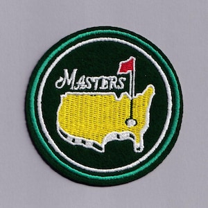 May include: A circular embroidered patch with the word "Masters" in white script above a yellow map outline with a red flag. The patch has a green border with white and green accents.