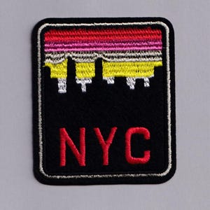 Puede incluir: Parche bordado negro con un diseño de horizonte en amarillo, rosa y rojo. El parche tiene un borde blanco y las letras "NYC" en rojo en la parte inferior. Ideal para personalizar ropa o accesorios.