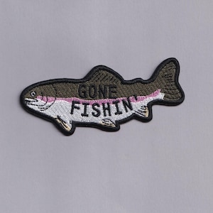 Puede incluir: Parche bordado con forma de pez con la frase "GONE FISHIN" en blanco. El pez tiene una parte superior verde oscuro, una franja rosa y un vientre blanco, delineado en negro. Para pescadores.