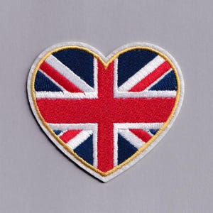 Puede incluir: Parche en forma de corazón con la bandera del Reino Unido, la Union Jack. El parche tiene un borde blanco con un ribete dorado. El diseño de la bandera incluye los colores rojo, blanco y azul.