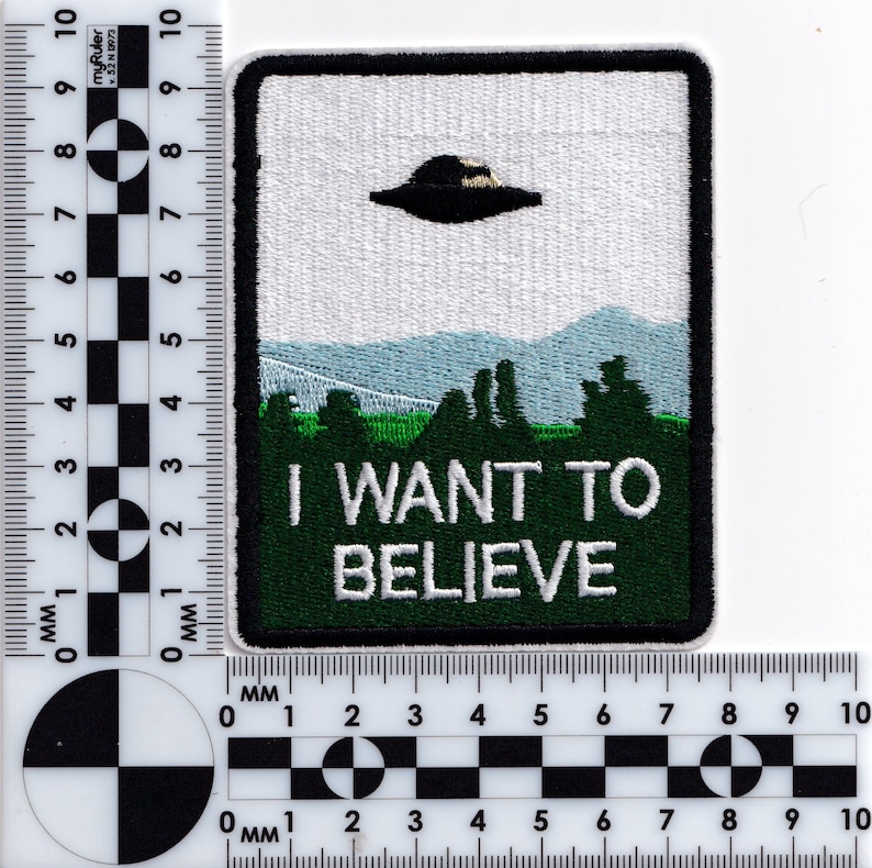 May include: Green embroidered patch with a white background. The patch features a flying saucer, a mountain range, and the text "I WANT TO BELIEVE".