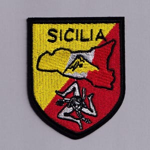 May include: Embroidered patch featuring the word "SICILIA" in yellow, above a map outline of Sicily in yellow and red. The patch includes a Trinacria symbol and a black border.