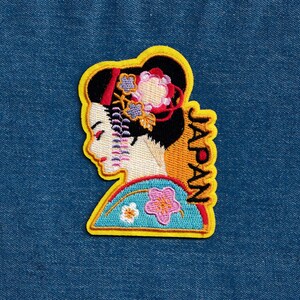 May include: Yellow embroidered patch featuring a geisha design and the word "JAPAN" in vertical script.