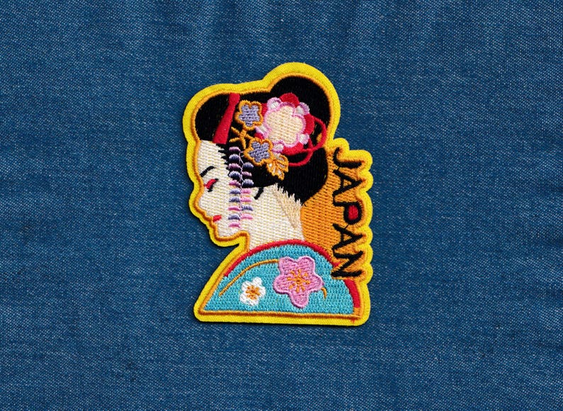 May include: Yellow embroidered patch featuring a geisha design and the word "JAPAN" in vertical script.