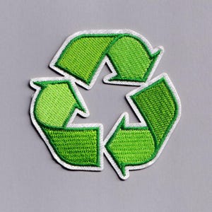 Puede incluir: Parche bordado con el símbolo de reciclaje universal. El diseño consta de tres flechas verdes que forman un triángulo, delineadas con costuras blancas. El parche está sobre un fondo gris.