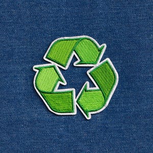 May include: Embroidered green recycling symbol patch with a white border, set against a blue denim background. The patch features a three-arrow design, representing the concept of reduce, reuse, and recycle.