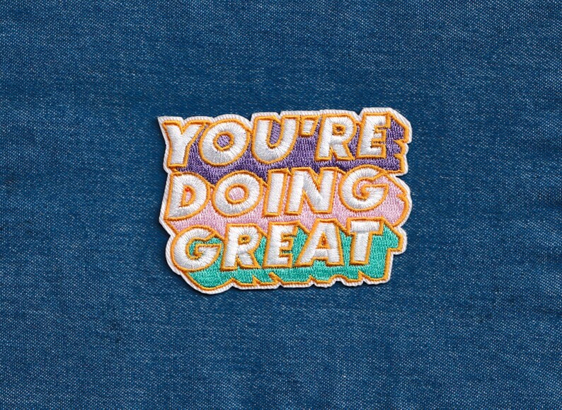 May include: A colorful embroidered patch with the text "You're doing great" in a retro font style. The patch is made of fabric and has a white outline.