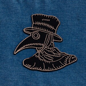 May include: Black and white embroidered patch of a plague doctor wearing a hat and mask.
