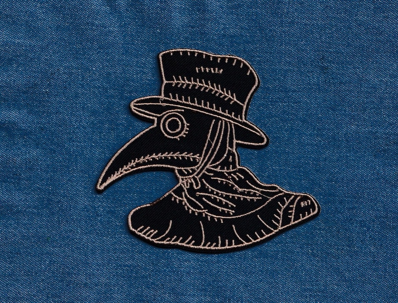 May include: Black and white embroidered patch of a plague doctor wearing a hat and mask.