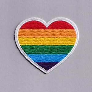 Può includere: Toppa ricamata a forma di cuore con un design arcobaleno. Presenta strisce rosse, arancioni, gialle, verdi, blu e viola, con un bordo bianco. Adatta per abbigliamento o accessori. Sfondo grigio.