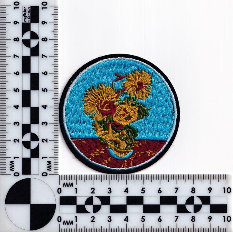 May include: Embroidered patch featuring a stylized depiction of sunflowers in a vase against a blue background. The vase is on a red and brown patterned surface.