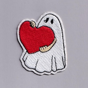 Op de afbeelding: Geborduurde patch met een witte geest die een groot rood hart vasthoudt. De geest heeft zwarte ogen en een zwarte mond. De patch heeft een witte achtergrond met een zwarte rand. Het hart is felrood van kleur.