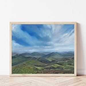 May include: Landscape painting of rolling green hills under a blue sky with white clouds. The artwork is framed in a light-colored wooden frame. The painting depicts a serene natural scene.