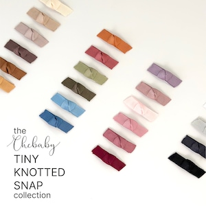 May include: A set of 14 tiny knotted hair clips in various colors, including beige, brown, green, blue, pink, red, and black. The clips are arranged in a diagonal line on a white background. The text "the Chebaby TINY KNOTTED SNAP collection" is visible in the lower left corner of the image.