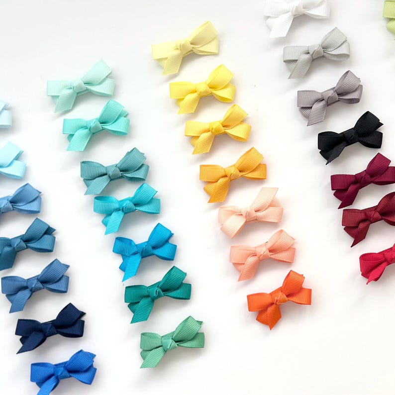 Puede incluir: Un surtido arco&iacute;ris de peque&ntilde;os lazos de tela hechos a mano. Los lazos est&aacute;n dispuestos en un patr&oacute;n de arco&iacute;ris, comenzando con azul claro y terminando con rojo. Todos los lazos miden aproximadamente 2,5 cm.