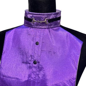 May include: A purple dickey with a high collar featuring a subtle tonal pattern and a black velvet ribbon trim. The collar is accented with a silver-toned metal horse bit detail. The front panel includes a vertical placket with two black buttons.