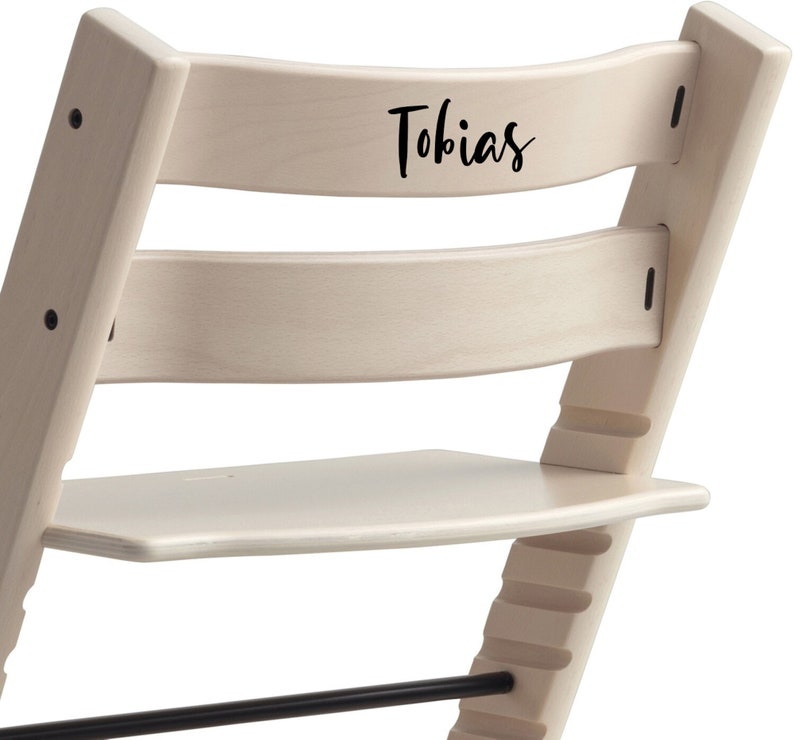 Puede incluir: Una silla alta de madera blanca con un reposapi&eacute;s negro y una placa de nombre negra en la parte posterior que dice "Tobias".