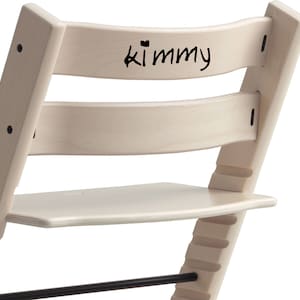 Puede incluir: Una silla de madera blanca con un reposapi&eacute;s negro y una inscripci&oacute;n negra en el respaldo que dice "Kimmy".