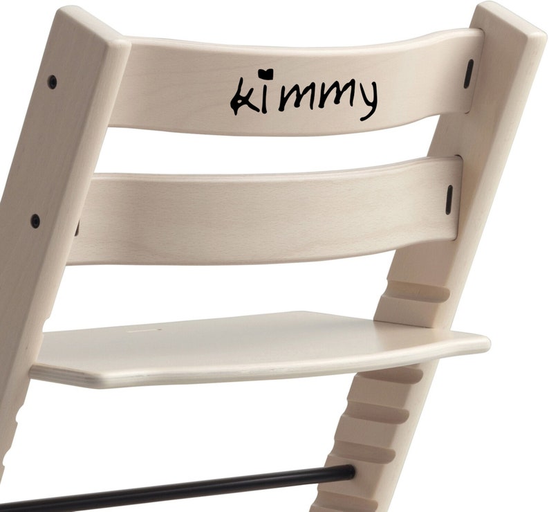Puede incluir: Una silla de madera blanca con un reposapi&eacute;s negro y una inscripci&oacute;n negra en el respaldo que dice "Kimmy".