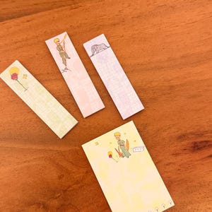 Könnte beinhalten: Eine Sammlung von Haftnotizen mit Illustrationen aus "Der kleine Prinz". Die Notizen sind rechteckig und haben Pastellfarben. Die Illustrationen zeigen den kleinen Prinzen, eine Rose und einen Elefanten.