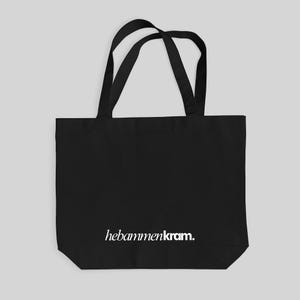 May include: A black tote bag featuring two shoulder straps and the white text hebammenkram. printed in a serif font near the bottom center. The bag has a rectangular body with a flat base and is constructed from a solid black fabric material.