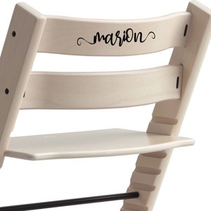 Puede incluir: Silla de madera blanca con un reposapi&eacute;s negro y una inscripci&oacute;n negra que dice "marion" en el respaldo.