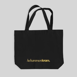 May include: A black tote bag with two shoulder straps and the text hebammenkram. printed in a gold-colored font near the bottom center. The bag features a rectangular body with a flat base and a simple, functional design for carrying items.