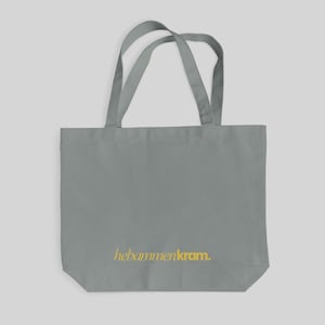 May include: A grey tote bag featuring two shoulder straps and the text hebammenkram. printed in yellow on the lower front section. The bag is constructed from a solid grey fabric with a rectangular shape and a flat base for storage.