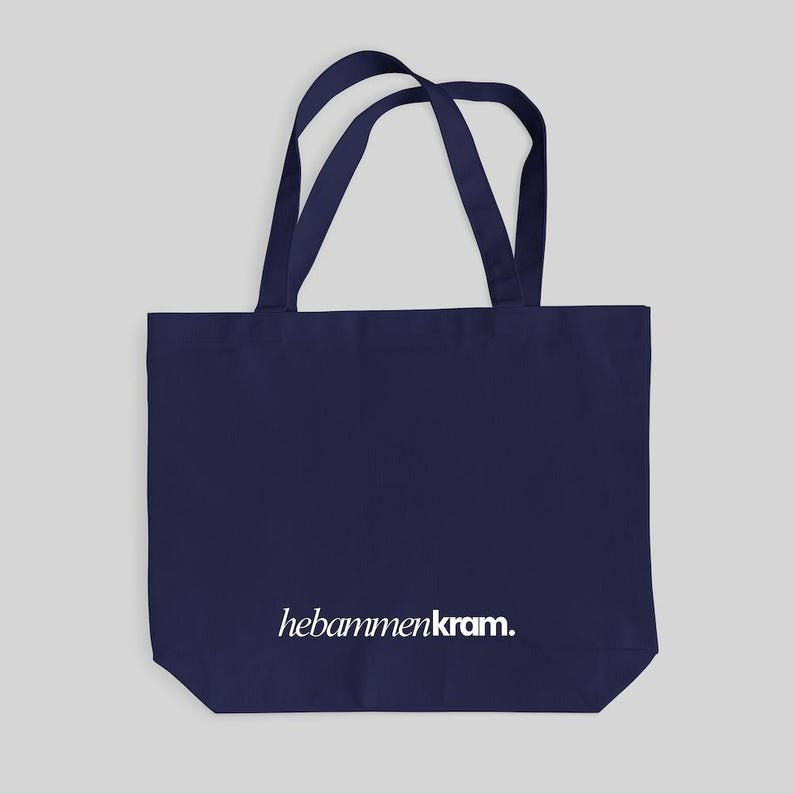 May include: A dark navy blue tote bag featuring two shoulder straps and the white text hebammenkram. printed in a lowercase serif font across the lower center portion of the bag. The bag has a rectangular shape with a flat bottom base.