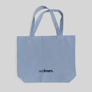 Puede incluir: Un bolso tote de color azul claro con dos asas a juego. El bolso presenta el texto "unikram." impreso en una fuente negra sencilla sin remates, centrado cerca de la parte inferior del panel frontal. El diseño es sencillo y funcional.