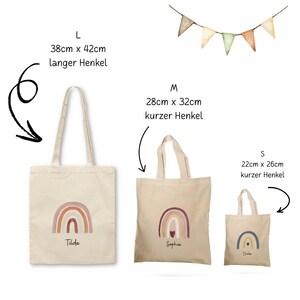 May include: Three beige canvas tote bags of varying sizes, each with a watercolor rainbow design. The largest bag is 38cm x 42cm, the medium bag is 28cm x 32cm, and the smallest is 22cm x 26cm. Each bag has a name printed below the rainbow.