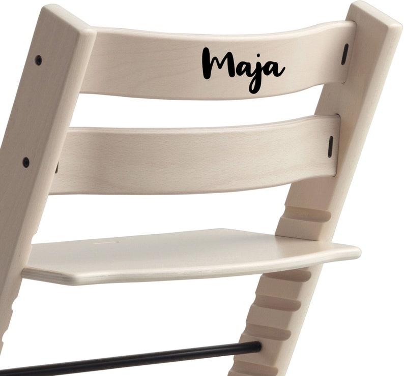 Puede incluir: Una silla de madera blanca con un reposapi&eacute;s negro y una etiqueta de nombre negra en la parte posterior que dice "Maja".