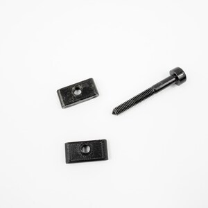 May include: Three black metal hardware pieces, including two rectangular brackets and a screw with a round head.