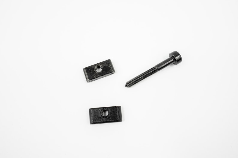 May include: Three black metal hardware pieces, including two rectangular brackets and a screw with a round head.