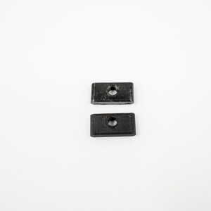 May include: Two black plastic rectangular blocks with a hole in the center.
